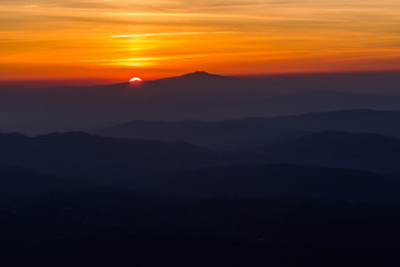 Beautiful sunset with sun coming down behind various layers of mountains