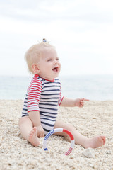 Adorable cheerful baby in striped bodysuit playing on the pebble beach