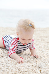 Adorable cheerful baby in striped bodysuit playing on the pebble beach