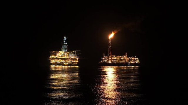 FPSO tanker vessel near Oil platform Rig. Offshore oil and gas industry, sea oil production and storage. Flare boom is brightly burning at night.
