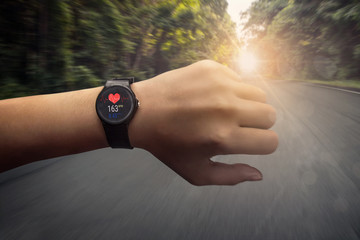 runner checking at heart rate monitor smart watch running on road in forest, color effect