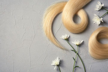 Composition with locks of blond hair and flowers on color background, flat lay. Space for text