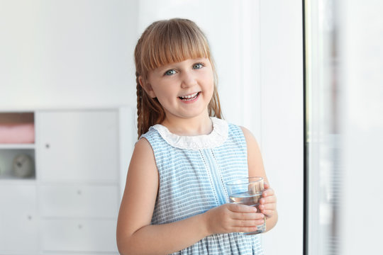 Cute little girl holding glass of fresh water at home