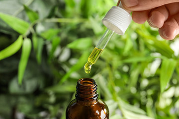 Woman holding pipette with oil over bottle on blurred background