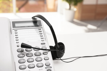 Headset and desk phone on table, space for text. Technical support concept