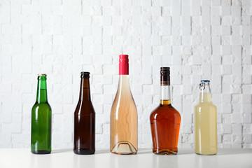 Bottles with different alcoholic drinks on table near white wall