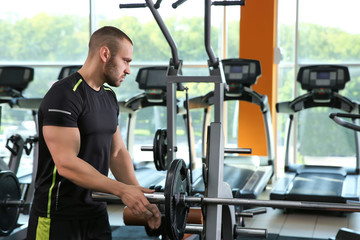 Strong young man near barbell in gym