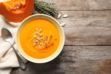 Flat lay composition with bowl of pumpkin soup and space for text on wooden background