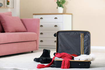 Modern suitcase with warm clothes on floor indoors. Space for text