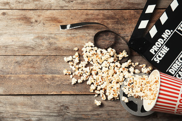 Tasty popcorn, film reel and clapperboard on wooden background, top view with space for text....