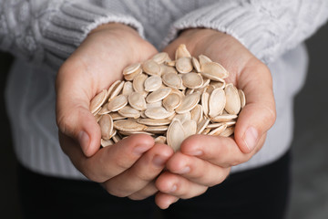 Woman holding raw pumpkin seeds, closeup view