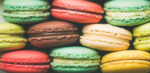 Flat-lay of sweet colorful French macaroon cookies stacked in rows, top view, wide composition