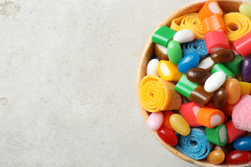 Bowl of delicious colorful candies on gray table, top view with space for text