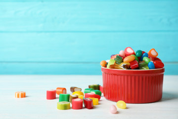 Bowl with delicious colorful candies on table against wooden background. Space for text
