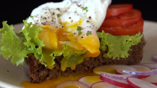 Poached egg on a piece of bread with green lettuce leaves and red tomato on a plate rotates, close up, breakfast concept