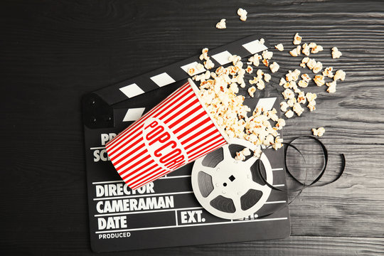 Tasty popcorn, film reel and clapperboard on wooden background, top view. Cinema snack
