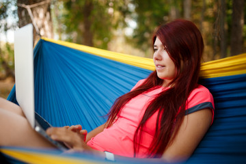 Photo on side of happy girl with laptop sitting in blue hammock