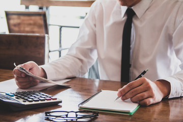 Asian young man in white shirt holding pen working ,Calculate tax lead to liquidation, With Sunset light vintage style.