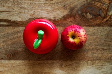 Fresh apple and ceramic apple side by side on wooden background.