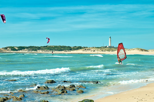 People surfing in front of the lighthouse of Trafalgar, on the beach of Los Caños de Meca, south of Spain