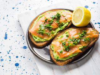 Rye bread avocado toasts with smoked salmon on white wooden board
