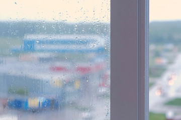 Raindrops flow down the window close-up. View of multi-building house from wet window, blur