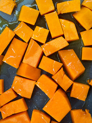 Chopped pumpkin being drizzled with olive oil before baking on a tin