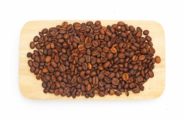 Many coffee beans are brown and have a pleasant aroma, on a wooden plate.