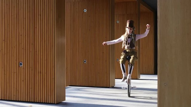 Girl clown rides a unicycle then juggling a bike outdoors
