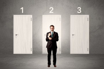 Businessman in grey room with three numbered white  door behind his back
