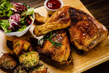 Grilled chicken legs with baked potatoes and vegetable salad on wooden table