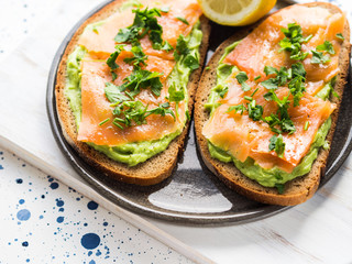 Rye bread avocado toasts with smoked salmon on white wooden board