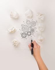 Female hand next to a few crumpled paper balls drawing rotating gears