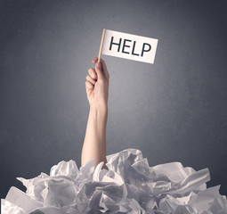 Female hand emerging from crumpled paper pile holding help sign 