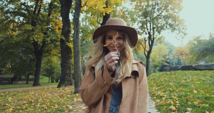 Rear of the Caucasian young attractive woman in a hat and coat having a walk in the park in autumn, turning to the camera and smiling. Back view. Portrait shot.
