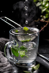 A cup of hot tea with mint leaves. Pouring fragrant hot with steam tea on a black background