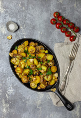 Russian freshness fried potatoes with mushrooms and onion in iron pan with fork and napkin at gray background. Salt near
