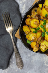 Rustic freshness fried potatoes with mushrooms and onion in iron pan with fork and napkin at gray background