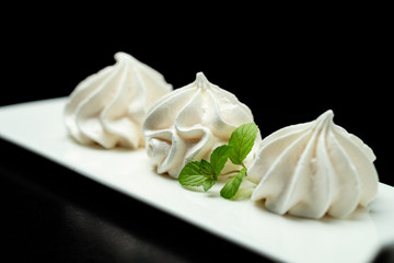 meringue meringue protein dessert in a white plate on a black background decorated with mint