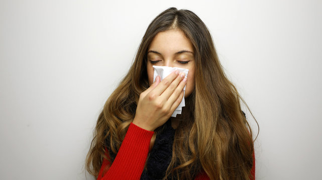 Portrait of a pretty woman having flu. girl blowing nose standing over gray background