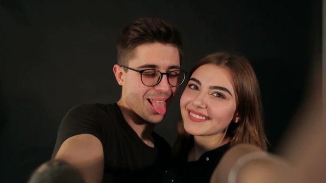 Portrait of two happy lovers making selfie on smartphone on black background. Happy hipster couple taking a selfie on black background. Shooting from the first person.
