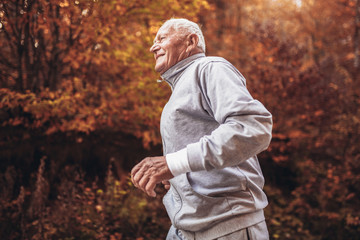 Senior runner in nature. Elderly sporty man running in forest during morning workout. Healthy and...