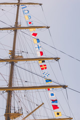 Fototapeta premium Colorful nautical sailing flags flying in the wind from the lines of a sailboat mast backlit in bright blue sky by the cloudy stormy day. Retro toned.