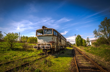Old locomotive in train cemetery in the summer with green grass and trees in the background and great cloudy sky