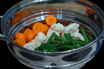 Vegetables in a stainless steel steamer prepared to be cooked with carrots, cauliflower and broccoli