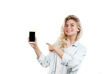 Fototapeta premium very beautiful young girl points to the smartphone, standing on a white isolated background.