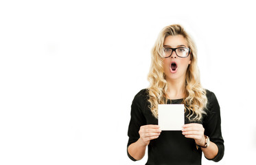 Naklejka premium Surprised emotional beautiful young girl holding a blank advertisement sheet on white isolated background. Black Friday, shopping, discounts