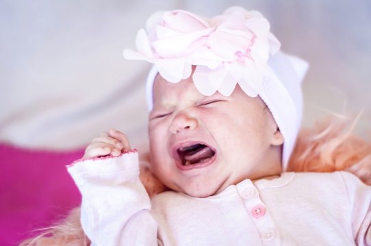 Cute newborn baby suffering from gas pain and crying. Gassy infant, colic gas treatment. Sad and upset infant concept image.