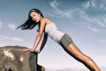 Strength training fitness woman working out core with angled push up exercise on rock. Asian athlete exercising with body weight exercises for toned body. Workout in summer desert landscape.