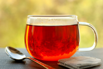 Hot tea and tea bag on the windowsill. A glass cup of tea, tea bag, dessert spoon against the window. Hot drink on the windowsill creates a cozy atmosphere.